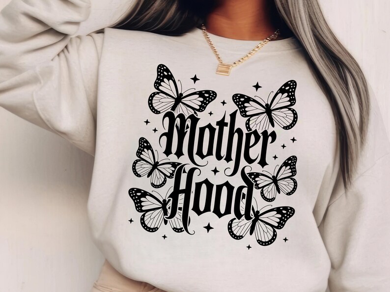 Puede incluir: Sudadera color crema con un dise&ntilde;o de mariposas y estrellas negras. Las palabras "Mother Hood" est&aacute;n escritas en una fuente g&oacute;tica. El dise&ntilde;o incluye seis mariposas y peque&ntilde;os acentos de estrellas.