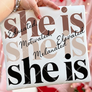 Può includere: Una tela quadrata bianca con le parole "she is" in grandi lettere nere. Sopra, le parole "Educated, Motivated, Elevated, Melanated" sono scritte in caratteri marroni e neri.