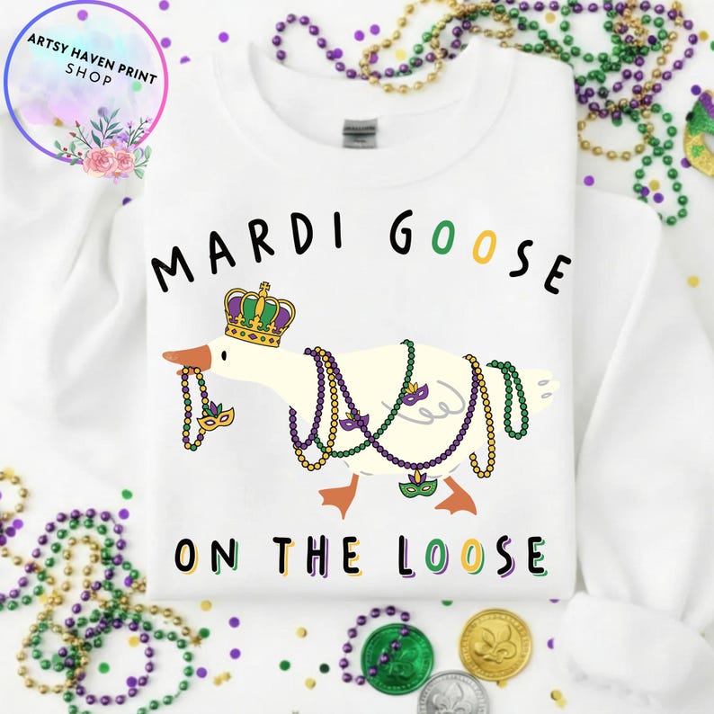 May include: White sweatshirt featuring a goose wearing a crown and Mardi Gras beads. The text "MARDI GOOSE ON THE LOOSE" is printed above and below the goose illustration. The sweatshirt has a crew neck.