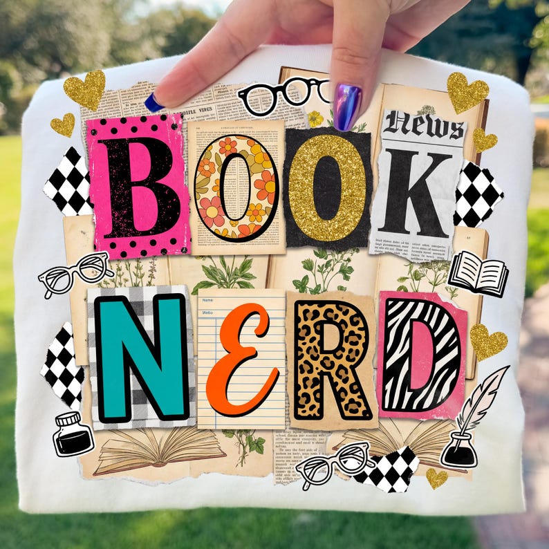 May include: A white t-shirt featuring the text "BOOK NERD" in a collage design. The letters are styled with diverse patterns and colours, such as pink polka dots, floral, gold glitter, and leopard print. Additional elements include hearts, glasses, and book illustrations.