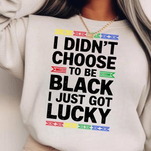 May include: White sweatshirt with a black graphic print that reads "I didn't choose to be black I just got lucky". The graphic is surrounded by colourful stripes.