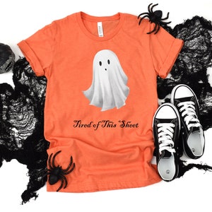 Peut inclure: T-shirt orange avec un motif de fantôme blanc et le texte "Tired of This Sheet".