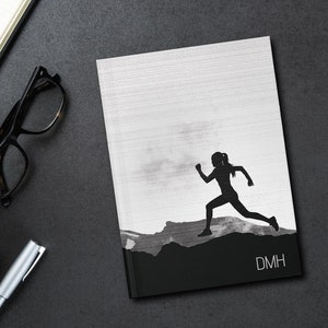 May include: A black and white notebook with a silhouette of a person running on a mountain. The notebook has the text "DMH" on the bottom right corner.