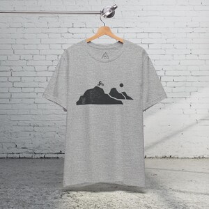 K&ouml;nnte beinhalten: Ein hellgraues T-Shirt mit einem Aufdruck eines Mountainbikers, der einen Berg hinauf f&auml;hrt, mit einer Sonne im Hintergrund.