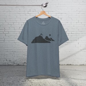 K&ouml;nnte beinhalten: Ein heidefarbenes T-Shirt mit einer schwarzen Grafik einer Bergkette und einer Person, die Fahrrad f&auml;hrt.