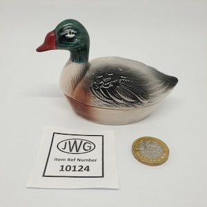 Peut inclure: Figurine de canard en céramique avec une tête verte, un bec rouge et un corps gris et blanc. Le canard est un objet décoratif. Une étiquette en papier avec le texte "JWG Item Ref Number 10124" est à côté du canard.