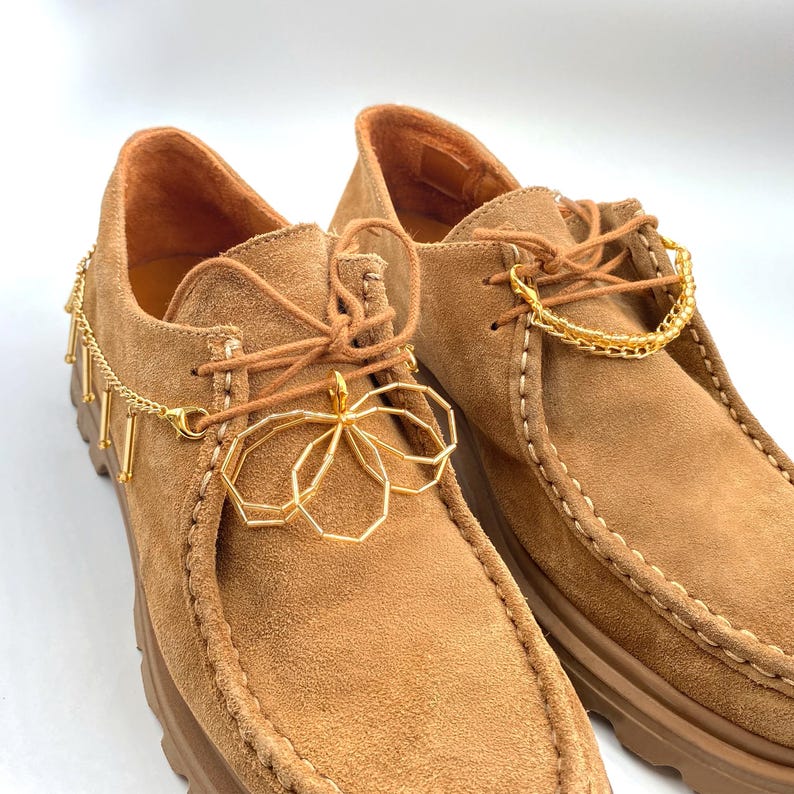 Gold chain and charm accessory on sneaker laces, ideal for a trendy, standout look.