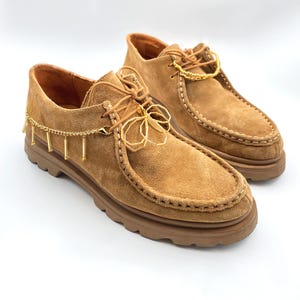 Gold shoelace charm on a gold chain, enhancing the look of casual footwear.