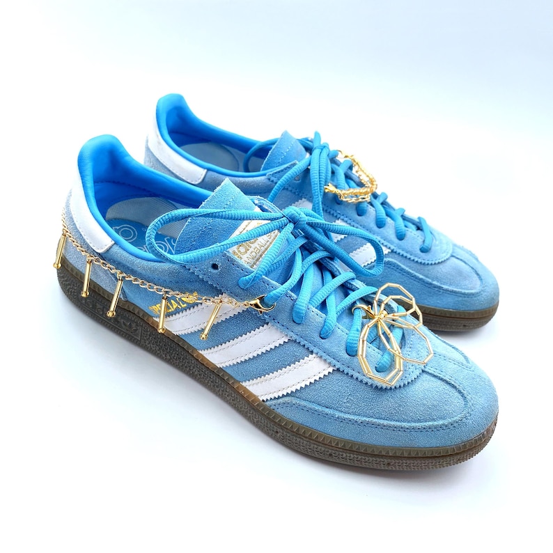 Stylish gold tassel charm chain with beads and flower charm attached to sneaker laces.