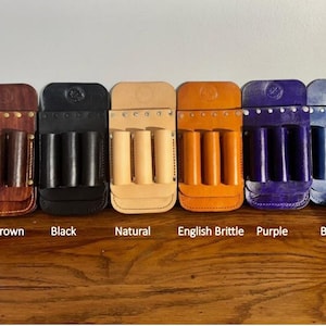 May include: Six leather tool holders in different colors: dark brown, black, natural, English brittle, purple, and blue. Each holder has three slots for tools.