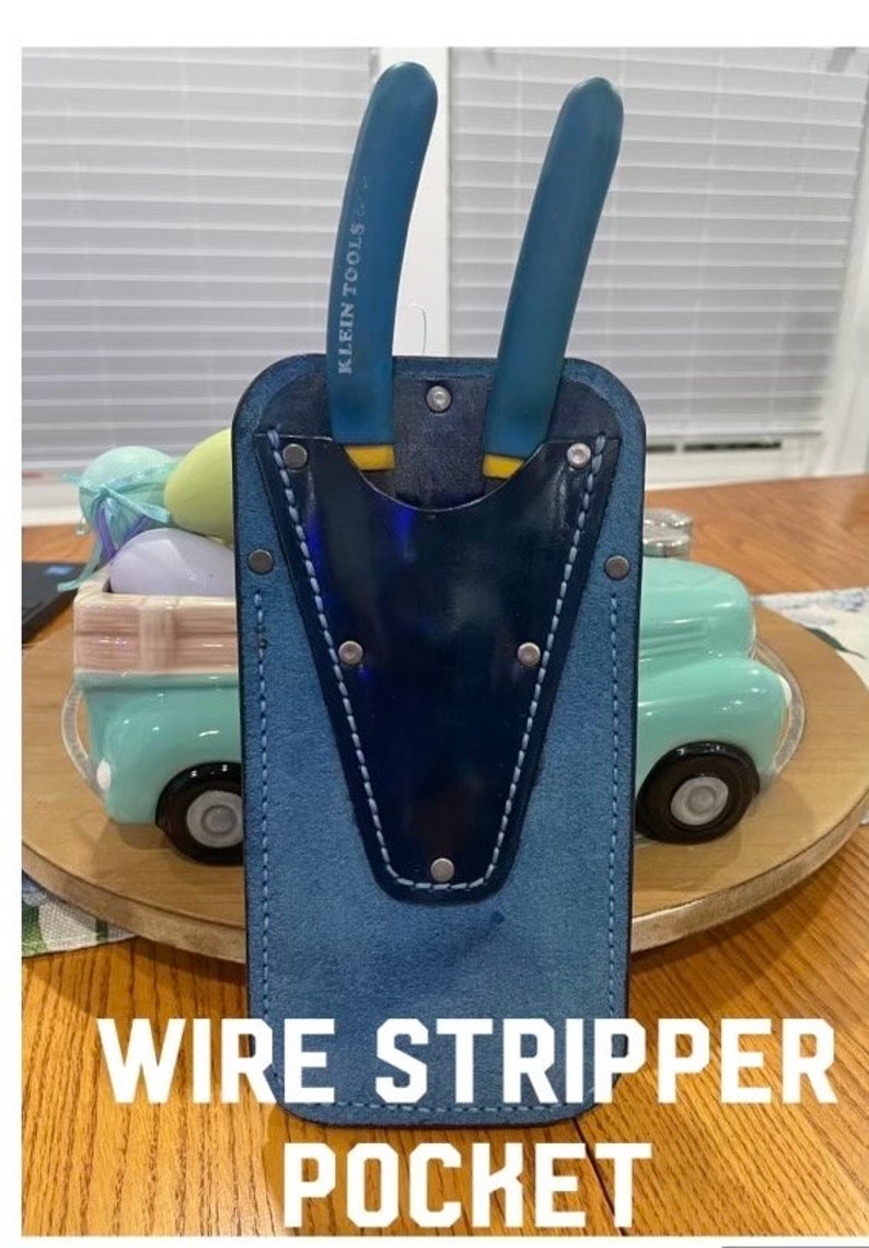 May include: A blue leather wire stripper pocket with a blue and white stitched pocket and two blue wire strippers with yellow handles. The strippers have the text "KLEIN TOOLS" printed on them. The pocket is labeled "WIRE STRIPPER POCKET".