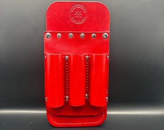 Può includere: Una custodia per cintura portautensili in pelle rosso vivo con tre tasche cilindriche. La custodia ha una chiusura a patta fissata con rivetti argentati. La patta superiore presenta un emblema circolare. La custodia è progettata per il trasporto di utensili.