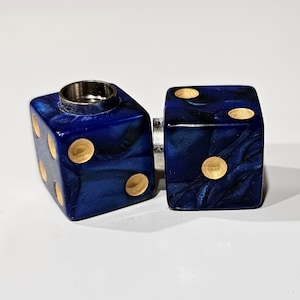 May include: Two blue dice with gold dots, one with a hole in the top, connected by a silver metal piece.