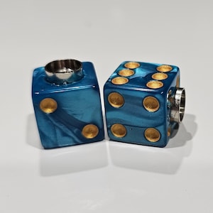 May include: Two blue dice with gold dots and a silver metal ring on top. The dice have a marbled effect with shades of blue and white. The dice are a unique and decorative item.