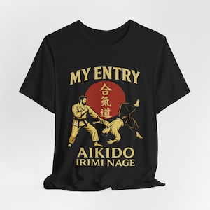 Könnte beinhalten: Schwarzes T-Shirt mit goldener und roter Grafik. Die Grafik zeigt zwei Figuren in Aikido-Stellungen, eine rote Sonne und den Text "MY ENTRY", "AIKIDO" und "IRIMI NAGE".