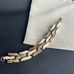 May include: A gold tone bracelet with a chain link design. The links are made of brown, white, and cream colored plastic.