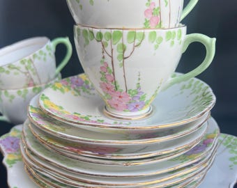 May include: A set of vintage teacups and saucers with a floral pattern. The cups and saucers are white with green leaves and pink, purple, and yellow flowers. The edges of the saucers are trimmed with gold.
