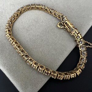 May include: A gold tennis bracelet with a row of clear round stones.