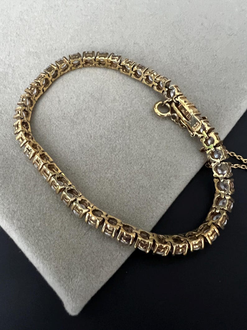 May include: A gold tennis bracelet with a row of clear round stones.