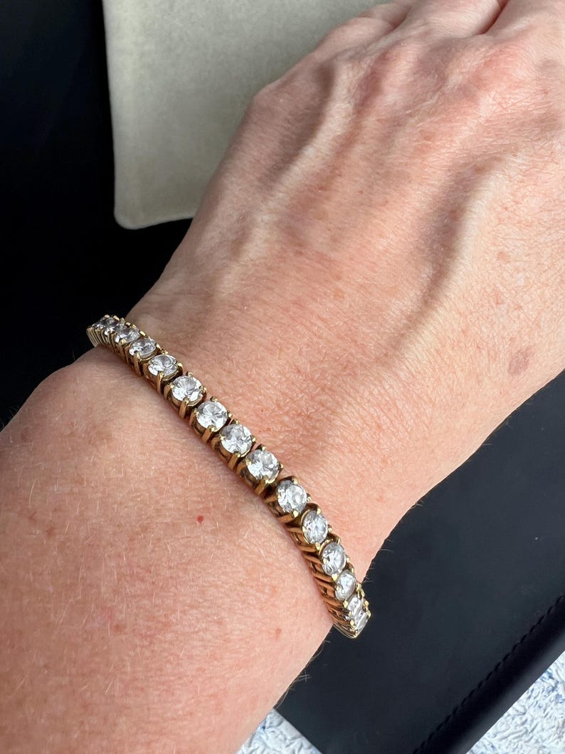 May include: A gold tennis bracelet with round clear stones.