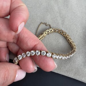 May include: A gold tennis bracelet with a row of round, clear diamonds.