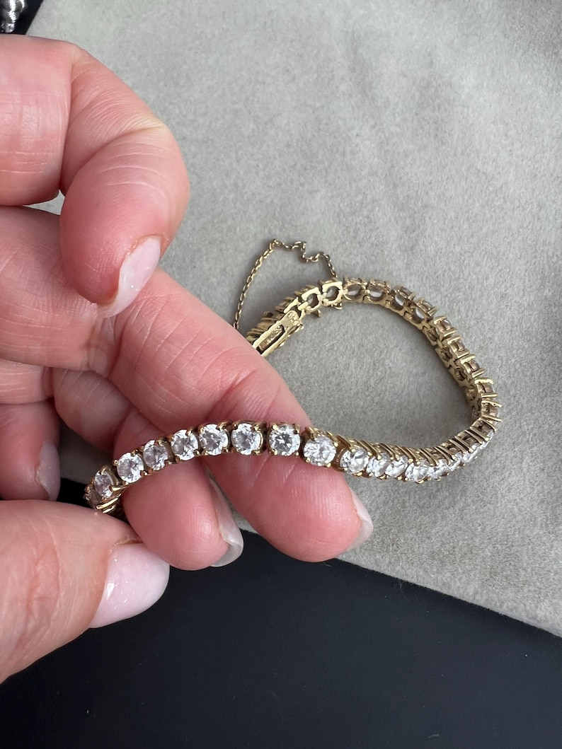 May include: A gold tennis bracelet with a row of round, clear diamonds.