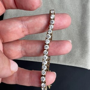 May include: A gold chain bracelet with round clear stones. The bracelet is on a person's hand.