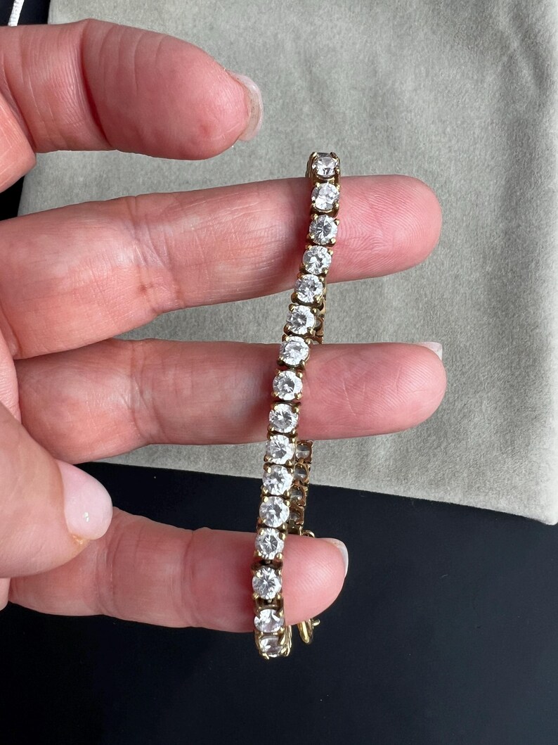 May include: A gold chain bracelet with round clear stones. The bracelet is on a person's hand.