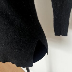 May include: A black sweater with a split hem and long sleeves. The sweater is made of a soft, textured material. The hemline is slightly curved, and the sleeves are long and fitted.