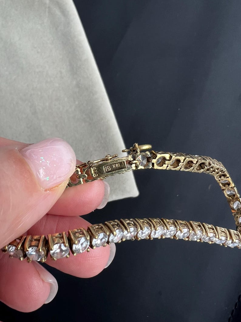 May include: A gold chain bracelet with small round clear stones. The clasp has the inscription "14K 585".