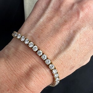 May include: A gold tennis bracelet with round clear stones.