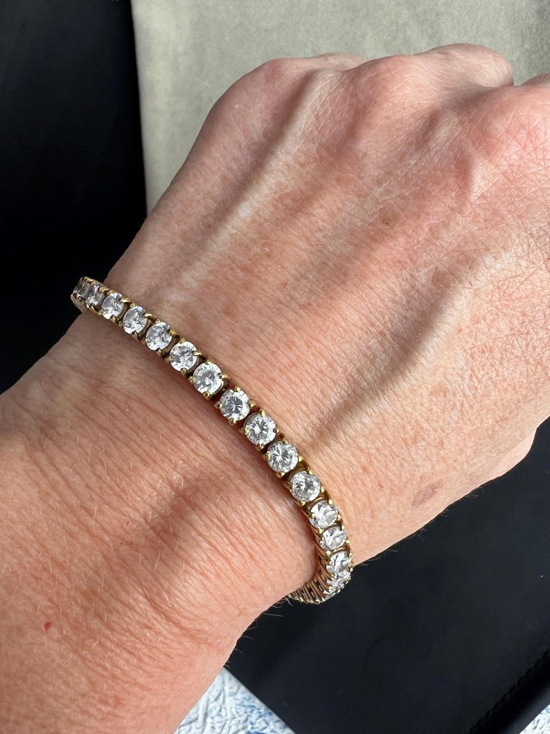 May include: A gold tennis bracelet with round clear stones.