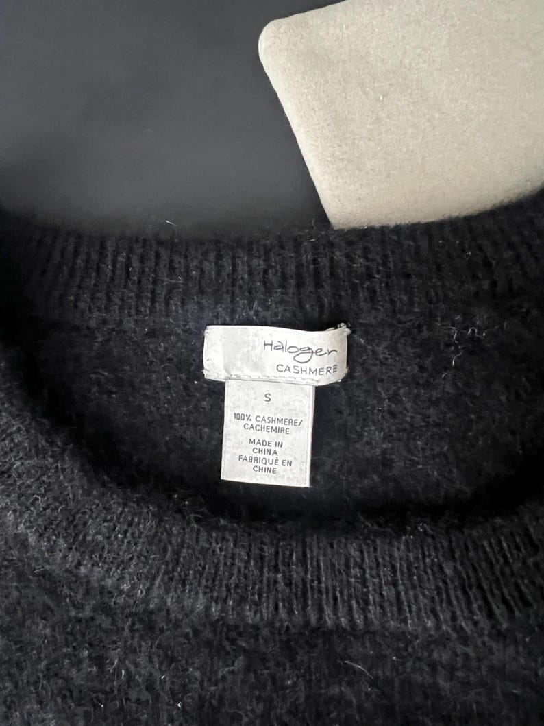 May include: Close-up of a black cashmere sweater. The tag reads "Halogen CASHMERE" and "100% CASHMERE/ CACHEMIRE". The tag also indicates the sweater is size "S" and "MADE IN CHINA / FABRIQU&Eacute; EN CHINE".