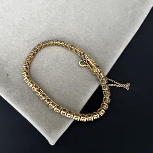 May include: A gold tennis bracelet with a row of clear stones.