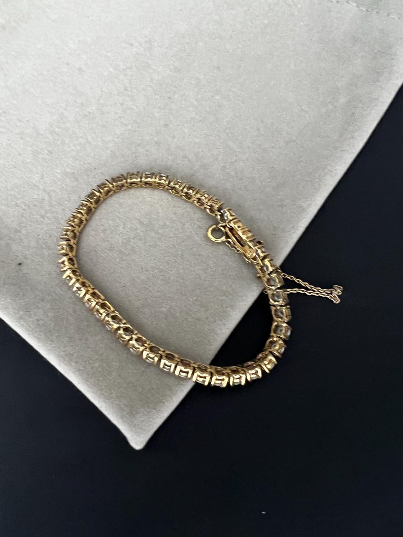 May include: A gold tennis bracelet with a row of clear stones.