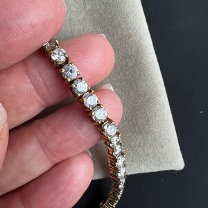May include: A gold tennis bracelet with a row of clear round cubic zirconia stones.