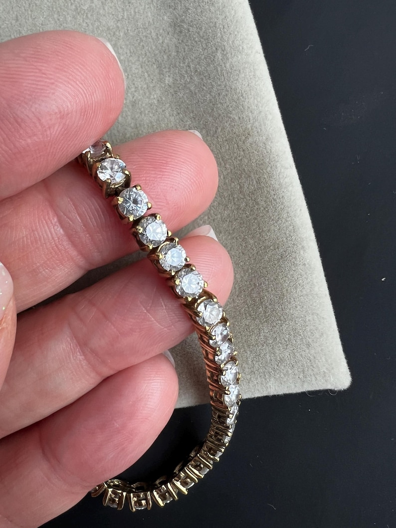 May include: A gold tennis bracelet with a row of clear round cubic zirconia stones.