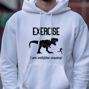 May include: White hooded sweatshirt with black text that reads "EXERCISE Some motivation required" and a black silhouette of a Tyrannosaurus Rex chasing a running person.