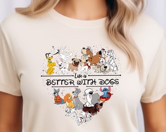 Puede incluir: Una camiseta de color crema con un diseño en forma de corazón que presenta varios perros de dibujos animados de películas de Disney. El texto "Life is Better With Dogs" está impreso en la camiseta.