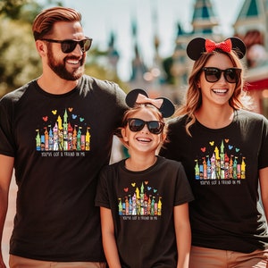 Op de afbeelding: Een gezin van drie personen draagt zwarte T-shirts met een kleurrijke illustratie van het Disney-kasteel en de tekst "You've got a friend in me".
