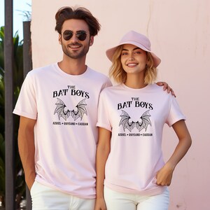 Puede incluir: Dos camisetas rosas con un gr&aacute;fico negro de alas de murci&eacute;lago y el texto "THE BAT BOYS" y "AZRIEL + RHYSAND + CASSIAN".