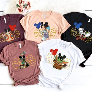 Pode incluir: Cinco camisetas diferentes com tema Star Wars com orelhas de Mickey Mouse e balões. As camisetas são de várias cores, incluindo vinho, pêssego, preto e branco. Cada camiseta apresenta um personagem diferente de Star Wars, incluindo a Princesa Leia, R2-D2, Yoda e Boba Fett.