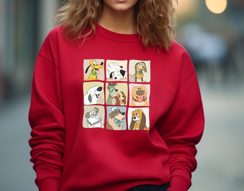Pu&ograve; includere: Una felpa rossa con una griglia di nove illustrazioni di cani dei cartoni animati. Ogni cane &egrave; in un quadrato separato, che mostra diverse razze ed espressioni. La felpa &egrave; di colore rosso tinta unita.