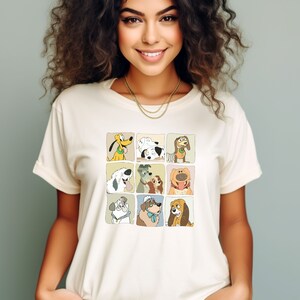 Pu&ograve; includere: T-shirt color crema con una griglia di nove illustrazioni di cani dei cartoni animati. I cani sono in singoli quadrati con un bordo marrone chiaro. La maglietta ha un girocollo classico e maniche corte.
