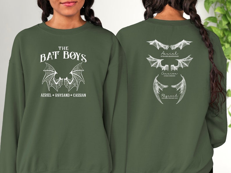 Puede incluir: Una sudadera verde con un estampado blanco de alas de murci&eacute;lago y el texto "THE BAT BOYS AZRIEL + RHYSAND + CASSIAN" en la parte delantera. La parte posterior de la sudadera tiene un estampado blanco de tres conjuntos de alas de murci&eacute;lago con los nombres "Azriel", "Cassian" y "Rhysand" escritos debajo de cada conjunto.