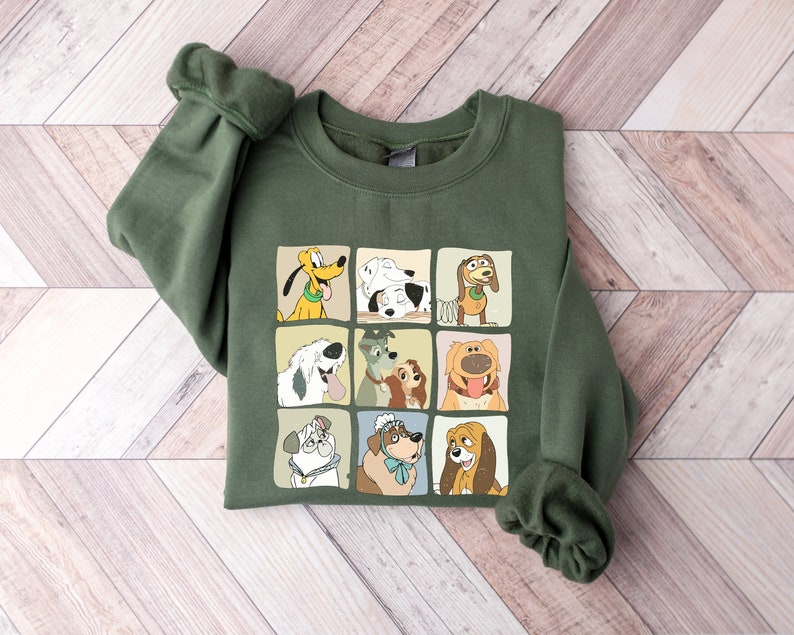 Pu&ograve; includere: Una felpa verde oliva con una griglia di personaggi di cani dei cartoni animati. Ogni cane &egrave; in un quadrato separato con uno sfondo color crema. La felpa ha maniche lunghe e girocollo.