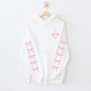 May include: White hoodie with a pink pixelated heart with a wifi symbol and power button on it. The sleeves have pink pixelated bows down the sides.