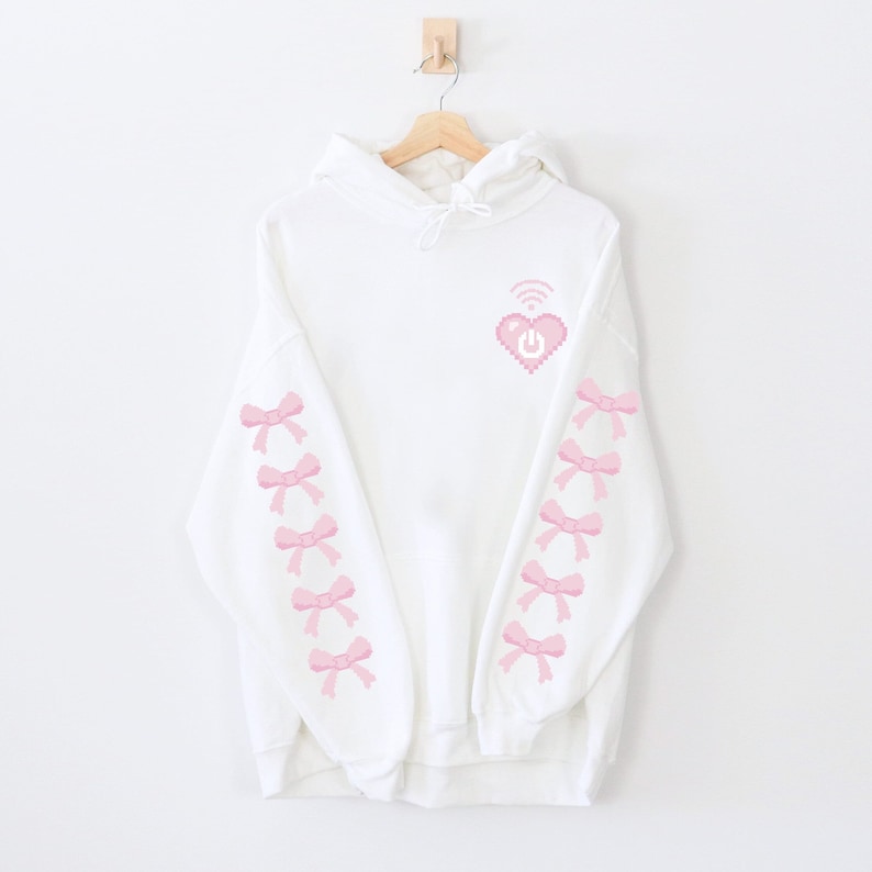 May include: White hoodie with a pink pixelated heart with a wifi symbol and power button on it. The sleeves have pink pixelated bows down the sides.