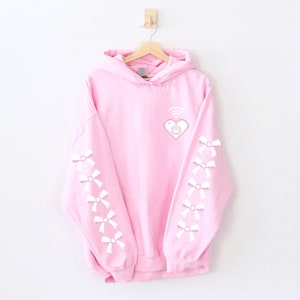 May include: A pink hoodie with a white pixelated heart with a wifi symbol and a power button inside. The sleeves have white pixelated bows.