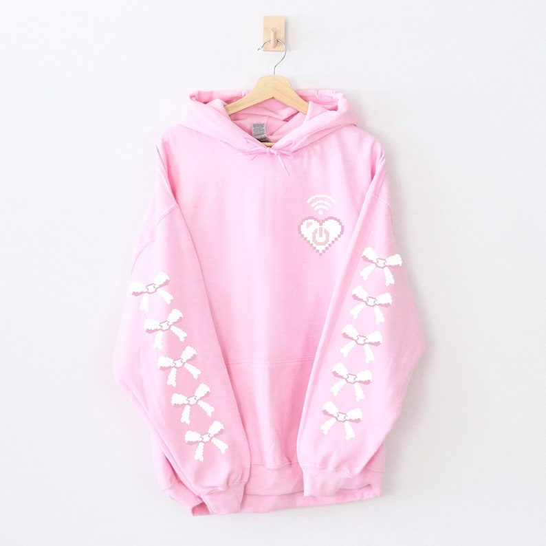 May include: A pink hoodie with a white pixelated heart with a wifi symbol and a power button inside. The sleeves have white pixelated bows.